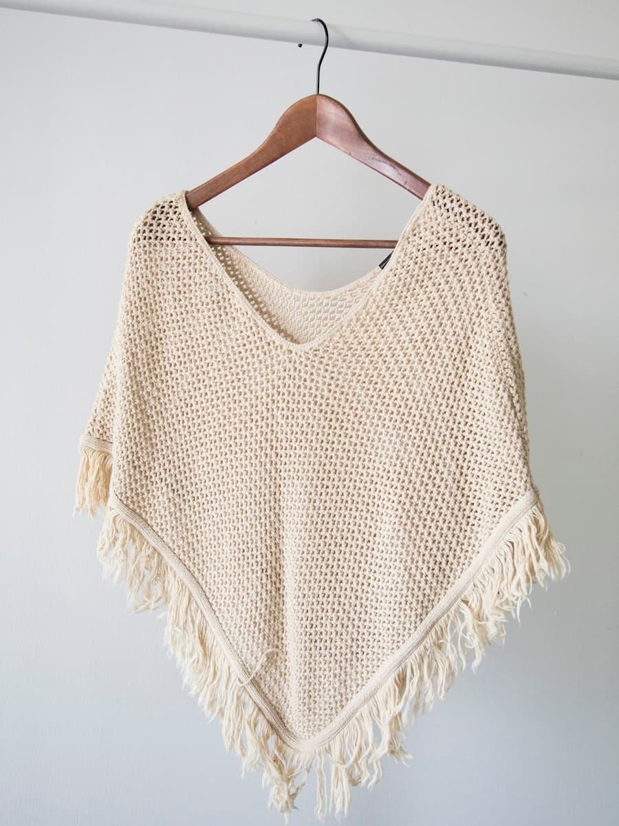 A cream hand-knit poncho on a wooden hanger
