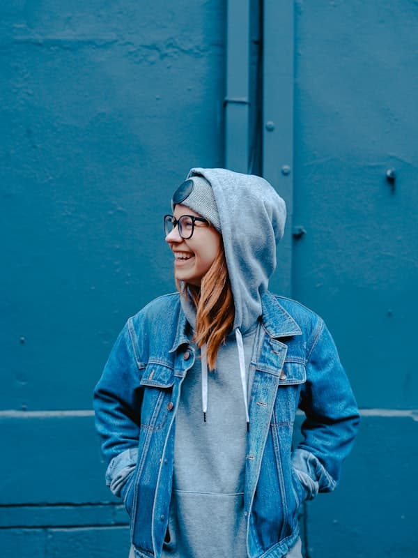 A woman in an oversized washed denim jacket over a grey hoodie