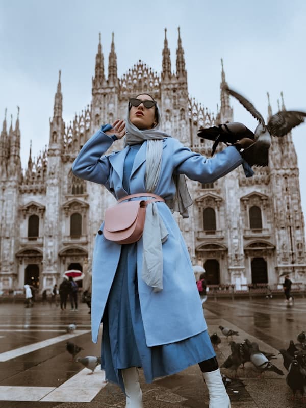 A woman in a pale blue belted wool coat on a city square