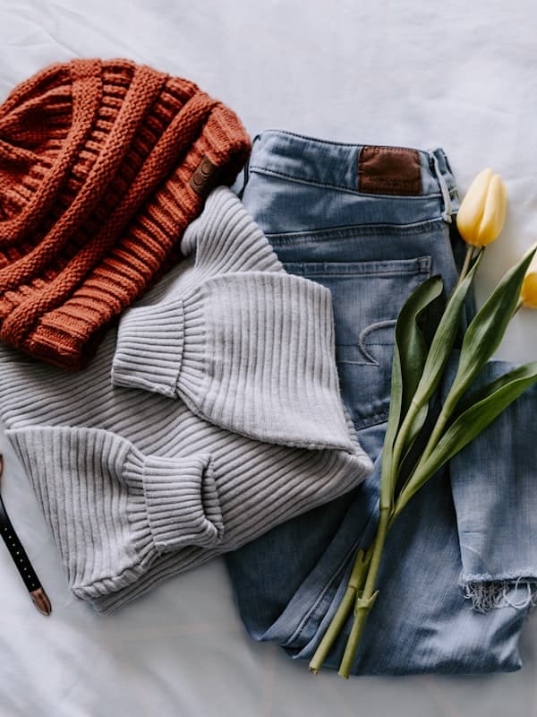 A folded grey knit, denim, and a rust beanie laid out with tulips