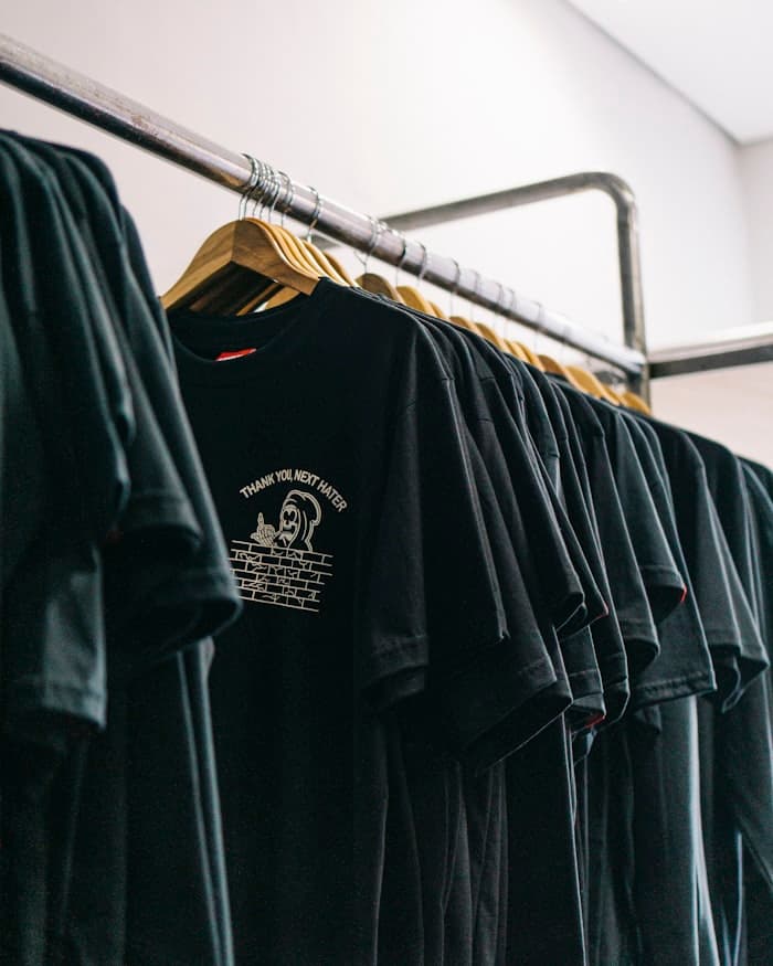 A rail of black cotton t-shirts on wooden hangers
